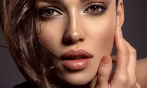 Close-up of a woman's face with dark eye makeup, glossy lips, and brown hair.