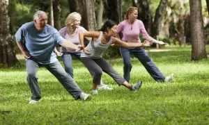 Gruppo di persone pratica tai chi in un parco, con movimenti fluidi e concentrati tra gli alberi.