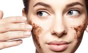 Viso di donna con scrub al caffè sulle guance. L'acido lattico a cosa serve? A esfoliare e rinnovare la pelle, rendendola luminosa.