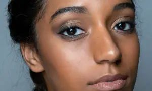 Primo piano di una donna con un intenso trucco occhi nero, labbra nude e pelle luminosa.