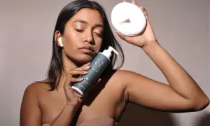 Donna con occhi chiusi tiene un latte detergente e un dischetto di cotone. Ricorda che il latte detergente va risciacquato per una pelle pulita.