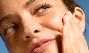 Dita accarezzano il viso per una pelle perfetta, illuminata dal sole.