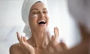 Donna con asciugamano in testa applica crema sul viso, gioia per il trattamento pelle grassa.