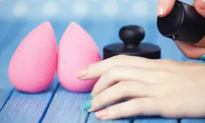 Due spugnette rosa e una mano con smalto colorato che applica fondotinta. Impara come lavare le beauty blender per mantenerle perfette.