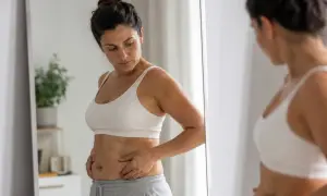 Donna si guarda allo specchio, preoccupata per la pancia e i fianchi, pensando a trattamenti estetici per ridurre queste zone.
