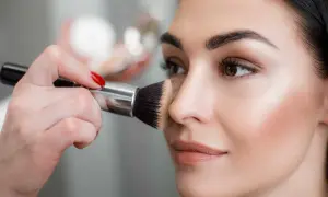 Mano con pennello applica terra sul viso per un look impeccabile.