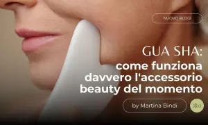 Un primo piano del viso di una donna con uno strumento **gua sha viso** bianco che scivola sulla sua guancia. Testo: "GUA SHA: come funziona davvero l'accessorio beauty del momento".
