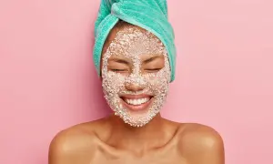 Donna con turbante e scrub sul viso, felice. Lo scrub viso serve a esfoliare e rinnovare la pelle, lasciandola luminosa e liscia.