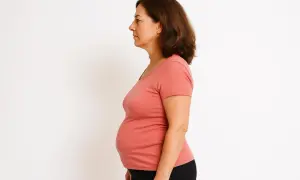 Donna vista di profilo, con evidente ingrasso solo sulla pancia. Indossa una maglietta corallo e pantaloni neri.