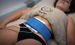 Donna sdraiata con dispositivo per la riduzione del grasso addominale. Opinioni sulla liposuzione non chirurgica.