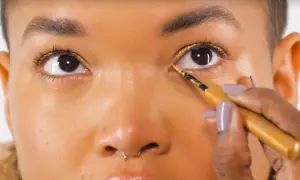 Occhi illuminati da un trucco oro e marrone scintillante, con eyeliner dorato applicato con precisione.