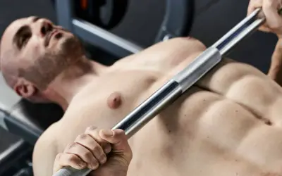 Uomo a petto nudo si allena con bilanciere, un passo fondamentale per chi vuole imparare come aumentare la massa muscolare.