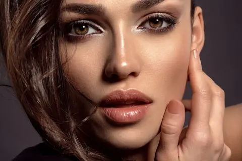 Close-up of a woman's face with dark eye makeup, glossy lips, and brown hair.