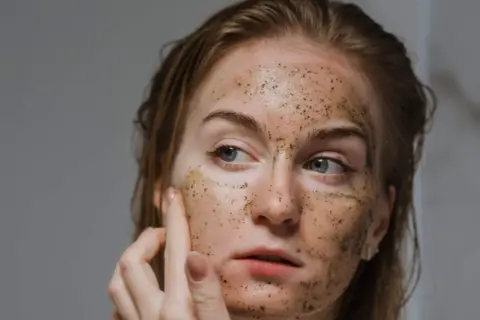 Donna si esfolia il viso con uno scrub, la pelle appare luminosa e rigenerata.