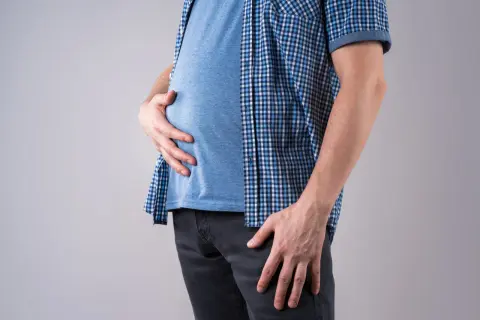 Uomo magro con pancia gonfia, che si tiene l'addome con le mani.