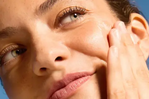 Dita accarezzano il viso per una pelle perfetta, illuminata dal sole.