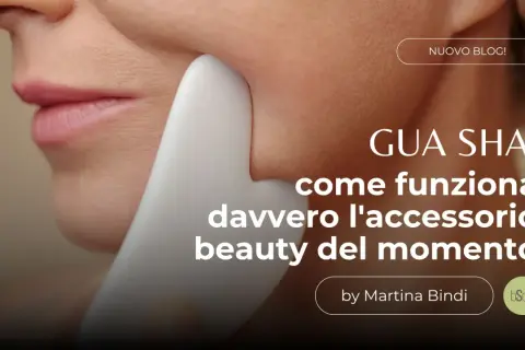 Un primo piano del viso di una donna con uno strumento **gua sha viso** bianco che scivola sulla sua guancia. Testo: "GUA SHA: come funziona davvero l'accessorio beauty del momento".