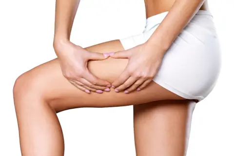 Mani che stringono la coscia, mostrando la texture della pelle. Un massaggio anticellulite doloroso per combattere gli inestetismi.