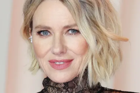 Primo piano di una donna con trucco palpebra cadente, labbra rosa e capelli biondi mossi.