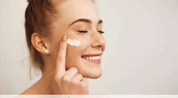 Donna sorridente applica latte detergente viso con la mano.
