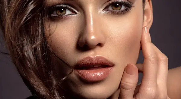 Close-up of a woman's face with dark eye makeup, glossy lips, and brown hair.