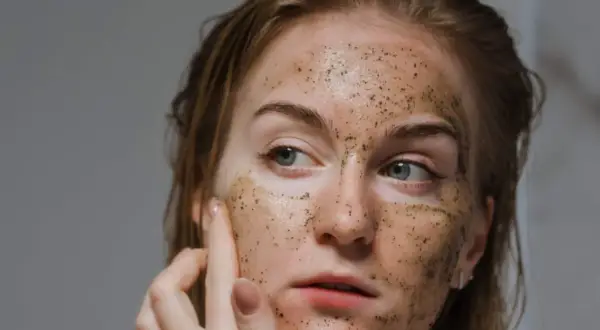 Donna si esfolia il viso con uno scrub, la pelle appare luminosa e rigenerata.