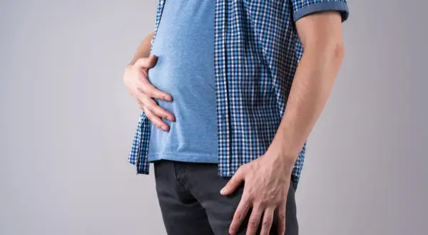 Uomo magro con pancia gonfia, che si tiene l'addome con le mani.