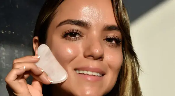 Donna sorridente con pietra gua sha rosa, mostrando un viso radioso e tonico, un effetto gua sha prima e dopo visibile.
