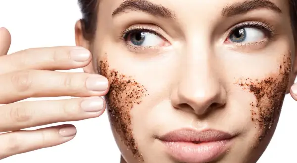 Viso di donna con scrub al caffè sulle guance. L'acido lattico a cosa serve? A esfoliare e rinnovare la pelle, rendendola luminosa.