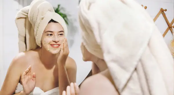 Ragazza con turbante applica una maschera sul viso, un gesto per come idratare la pelle e renderla luminosa.