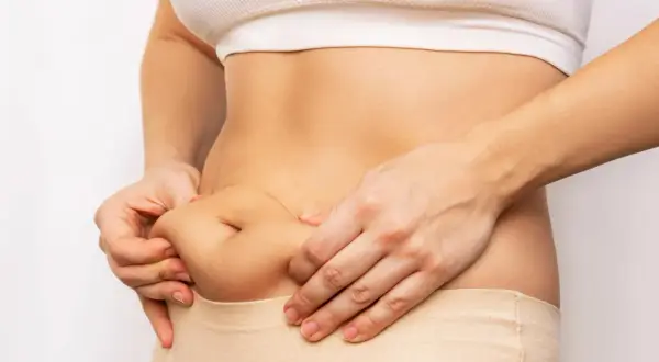 Mani che stringono il fianco, mostrando accumuli di grasso. Il cortisolo gonfia, evidenziando la necessità di uno stile di vita sano.
