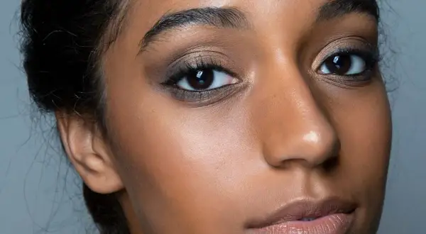 Primo piano di una donna con un intenso trucco occhi nero, labbra nude e pelle luminosa.