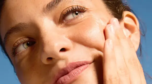 Dita accarezzano il viso per una pelle perfetta, illuminata dal sole.