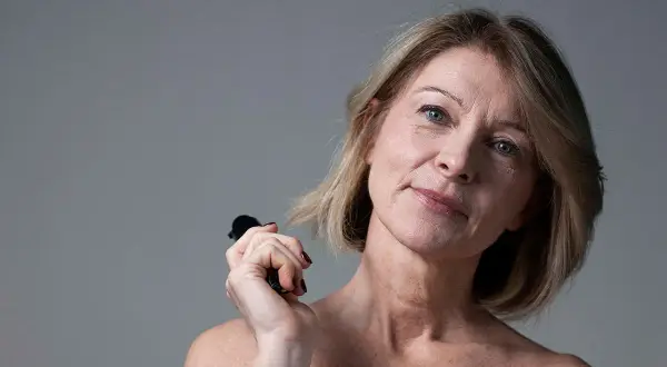 Donna con pelle cadente sotto il mento, che tiene un piccolo oggetto nero. Scopri i rimedi per la pelle cadente sotto il mento.