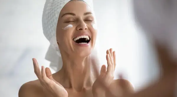 Donna con asciugamano in testa applica crema sul viso, gioia per il trattamento pelle grassa.