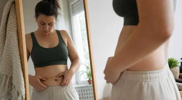 Donna si guarda allo specchio, toccando le parti della pancia.
