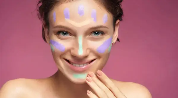 Ragazza sorridente con correttori colorati sul viso, un esempio visivo per capire come scegliere il correttore giusto per ogni imperfezione.