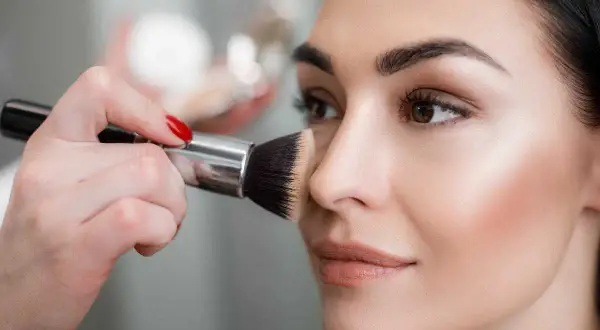 Mano con pennello applica terra sul viso per un look impeccabile.