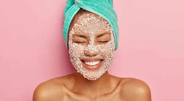 Donna con turbante e scrub sul viso, felice. Lo scrub viso serve a esfoliare e rinnovare la pelle, lasciandola luminosa e liscia.