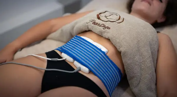 Donna sdraiata con dispositivo per la riduzione del grasso addominale. Opinioni sulla liposuzione non chirurgica.