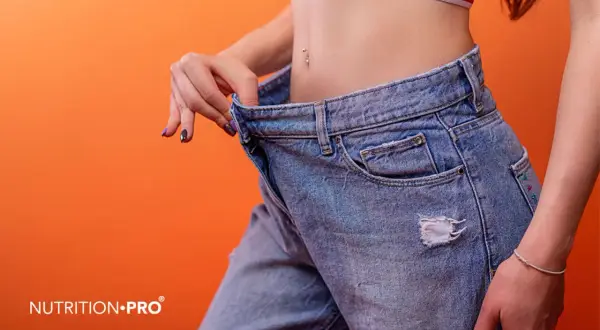 Donna mostra jeans larghi, segno di successo nel come appiattire la pancia. Un risultato visibile di un percorso di benessere.