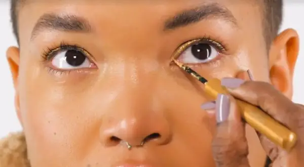 Occhi illuminati da un trucco oro e marrone scintillante, con eyeliner dorato applicato con precisione.