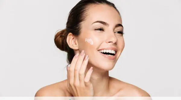 Donna sorridente applica crema sul viso. Il doposole serve a lenire e idratare la pelle dopo l'esposizione al sole, mantenendola morbida e sana.