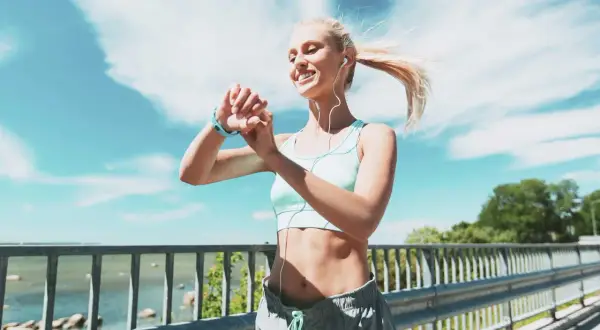 Donna bionda con smartwatch e auricolari controlla i suoi progressi, ideale per dimagrire meglio correre o camminare.