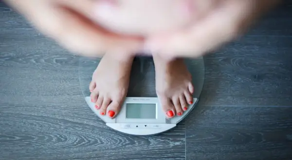 Piedi su una bilancia digitale, con smalto rosso vivo. La persona sembra preoccupata per un possibile aumento di peso improvviso.