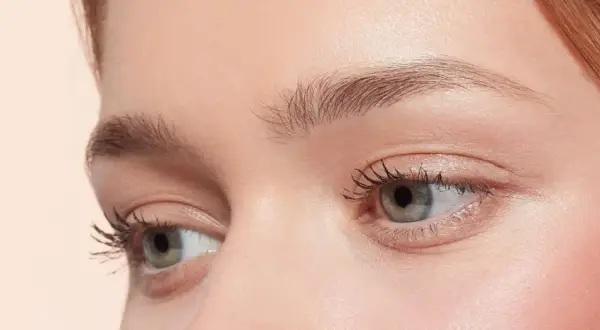 Occhi verdi con ciglia lunghe e folte, sopracciglia curate e un tocco di blush. Un look make up nude che esalta la bellezza naturale.