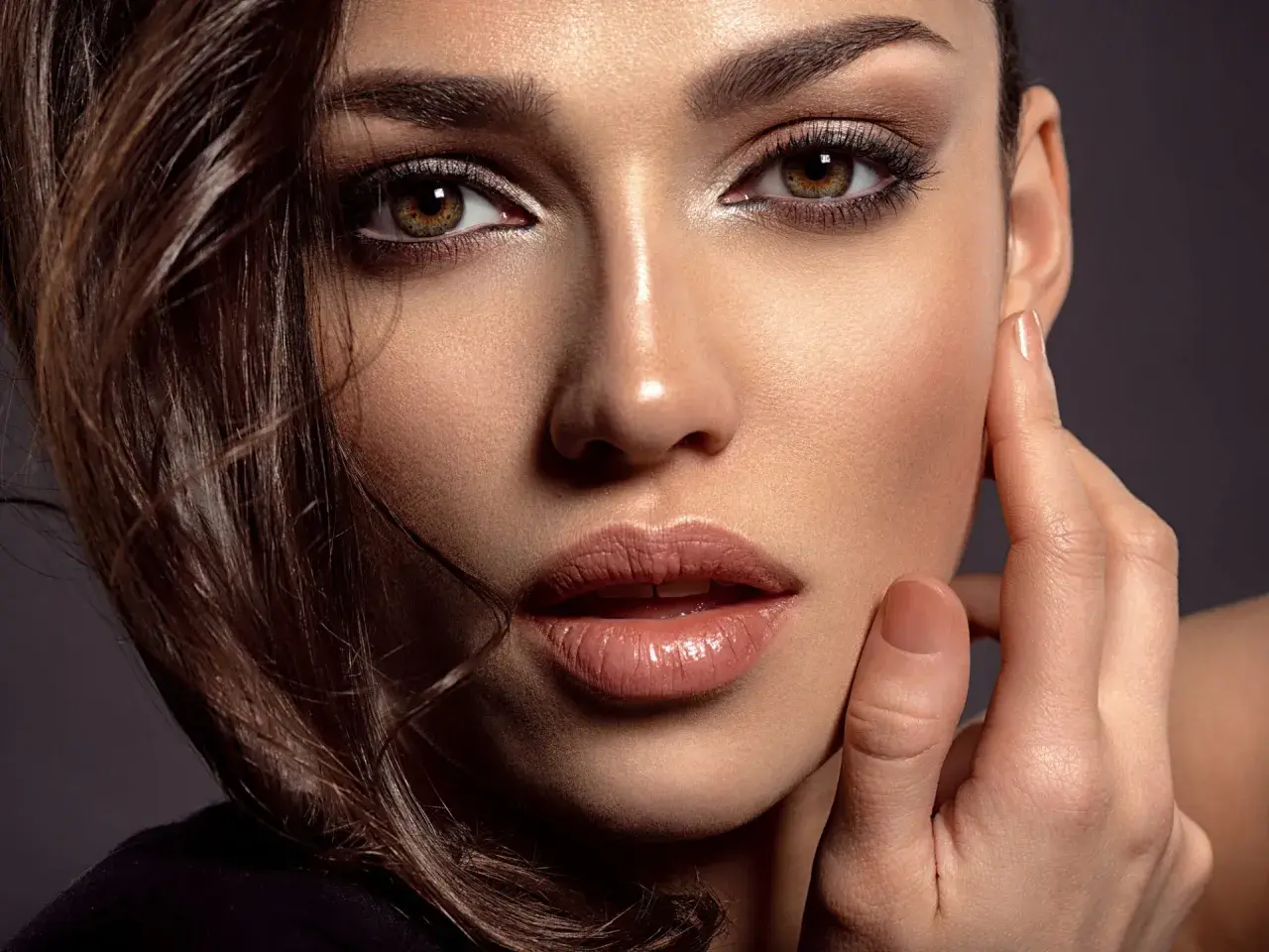 Close-up of a woman's face with dark eye makeup, glossy lips, and brown hair.
