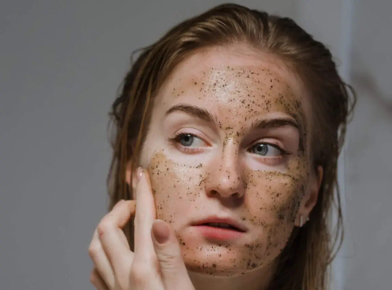 Donna si esfolia il viso con uno scrub, la pelle appare luminosa e rigenerata.