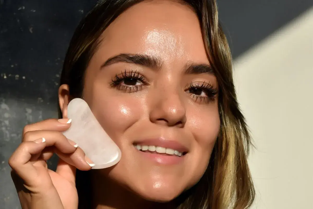 Donna sorridente con pietra gua sha rosa, mostrando un viso radioso e tonico, un effetto gua sha prima e dopo visibile.
