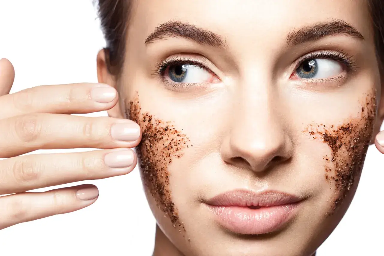 Viso di donna con scrub al caffè sulle guance. L'acido lattico a cosa serve? A esfoliare e rinnovare la pelle, rendendola luminosa.